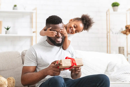 Girl covering dad’s eyes while he holds a present