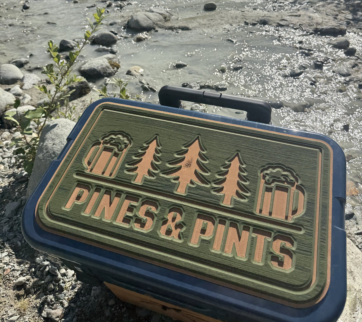 Pines & Pints custom logo cooler top pad on a navy cooler by a mountain river