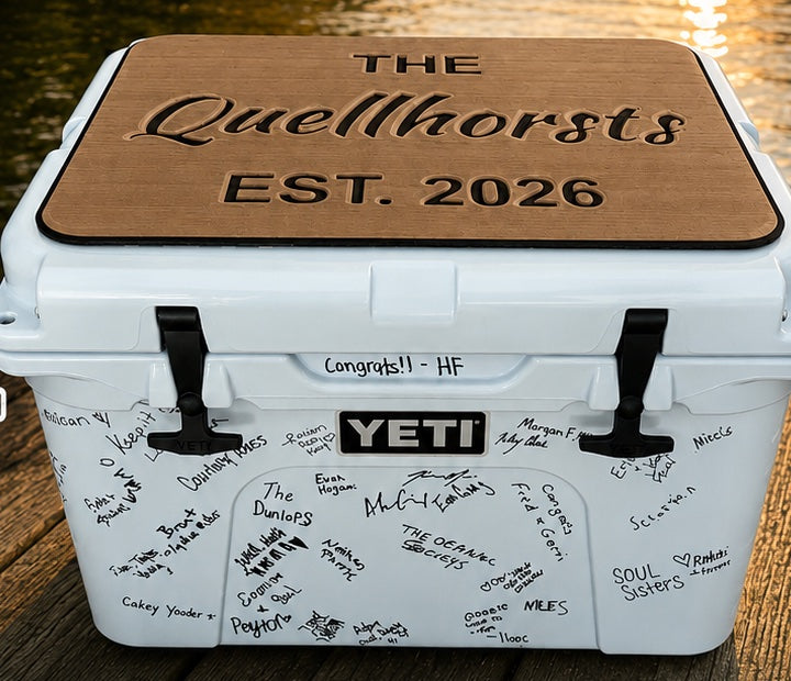The Quellhorsts Est. 2026 teak cooler top pad on a wedding guest book Yeti cooler